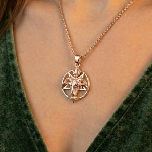 A close-up of a person wearing a gold-colored pendant necklace with a circular design.