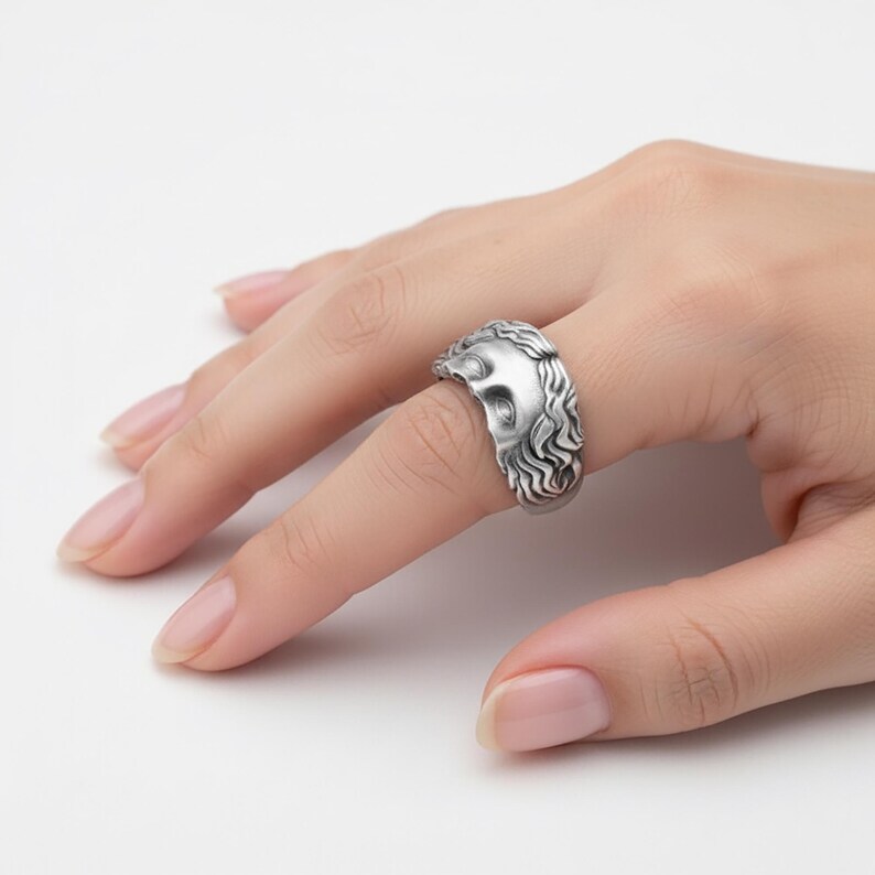A close-up view of a person's hand wearing a silver ring with an intricate design.