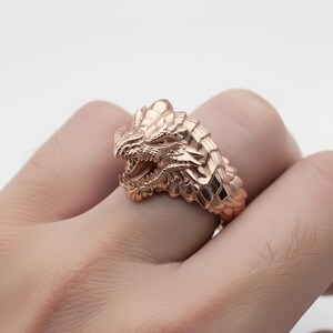 A close-up image of a person's hand wearing a gold-colored dragon ring.