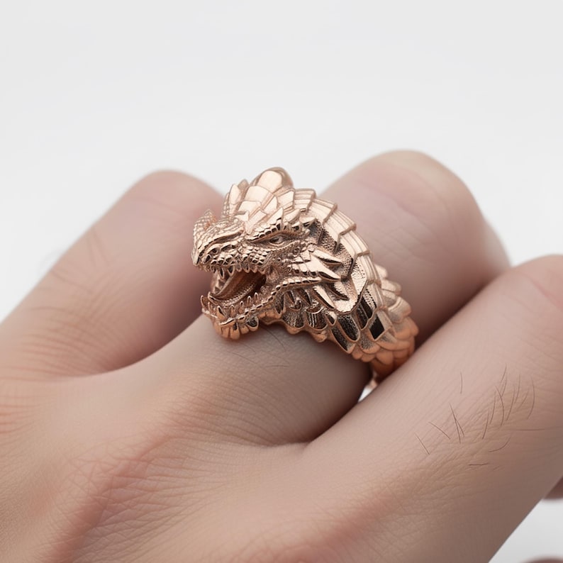 A close-up image of a person's hand wearing a gold-colored dragon ring.