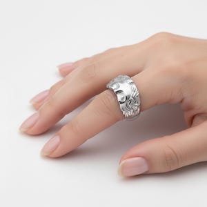 A close-up view of a person's hand wearing a silver ring with an intricate design.