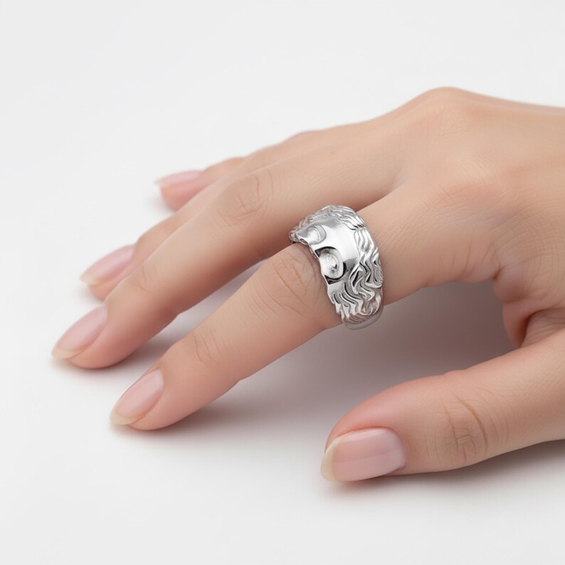 A close-up view of a person's hand wearing a silver ring with an intricate design.