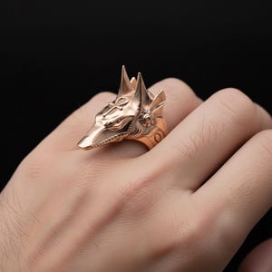 A close-up image of a person's hand wearing a gold-colored ring featuring a detailed design of a fox's head.