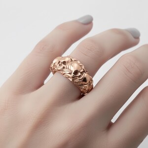 A close-up of a person's hand wearing a gold ring with an intricate design featuring multiple skull motifs.