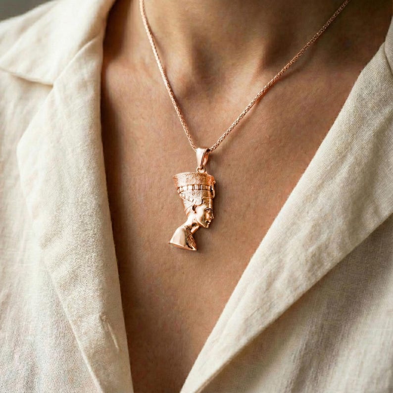 A close-up of a person wearing a gold-colored pendant necklace with a pendant depicting a female figure.