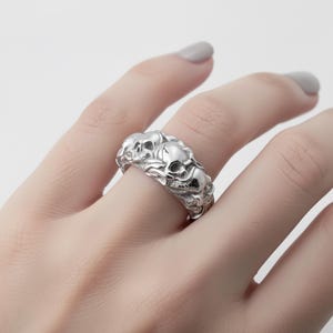 A close-up of a silver ring with a skull design on the finger.