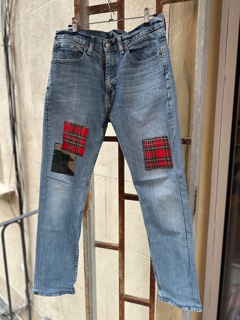 Może przedstawiać: Dżinsy z niebieskiego denimu z czerwonymi i czarnymi łatkami w kratę na przodzie każdej nogawki.