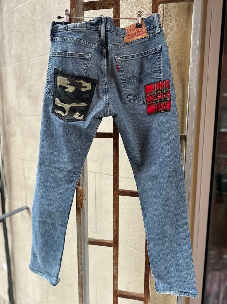 Może przedstawiać: Dżinsy z niebieskiego denimu z naszywką z tkaniny maskującej na tylnej lewej kieszeni i naszywką z czerwono-czarnej tkaniny w kratę na tylnej prawej kieszeni.