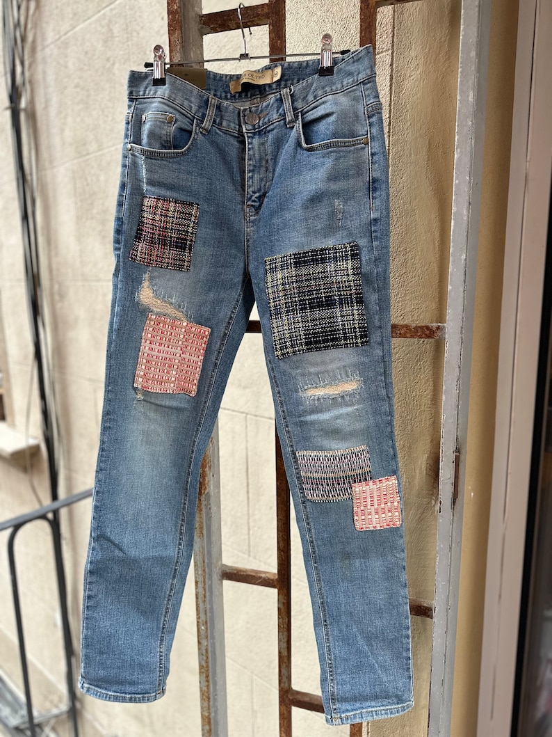 Może przedstawiać: Dżinsy z niebieskiego denimu z detalami w postaci patchworku. Łaty wykonane są z r&oacute;żnych tkanin i kolor&oacute;w, w tym czerwonego, czarnego i białego. Dżinsy mają przetarty wygląd z rozdarciami i dziurami.