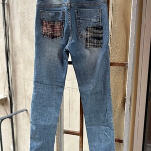 Może przedstawiać: Dżinsy z niebieskiego denimu z dwoma naszywkami z tkaniny w kratę na tylnych kieszeniach.