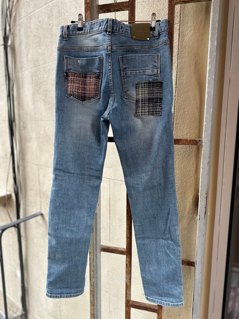 Może przedstawiać: Dżinsy z niebieskiego denimu z dwoma naszywkami z tkaniny w kratę na tylnych kieszeniach.