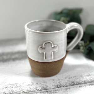 May include: White ceramic mug with a brown base and a raised cross design.