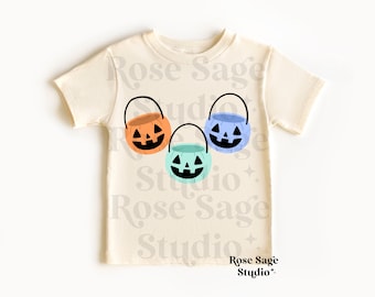 May include: A white t-shirt with three pumpkin-shaped trick-or-treat buckets. The buckets are orange, blue, and green.