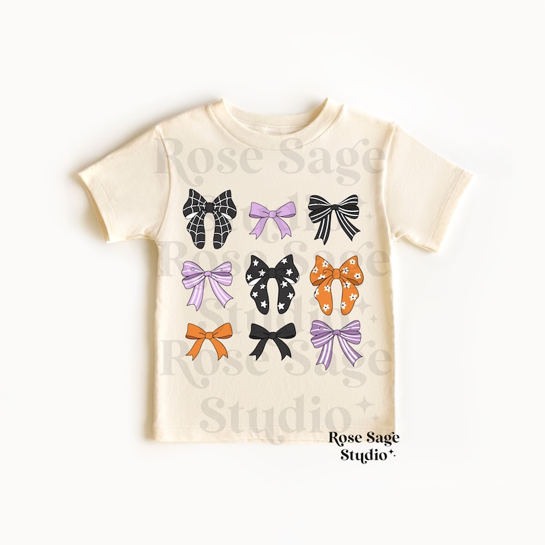 Pode incluir: Uma camiseta cor creme com um gr&aacute;fico de nove la&ccedil;os diferentes em preto, laranja, roxo e branco. Os la&ccedil;os est&atilde;o dispostos em um padr&atilde;o de grade. O texto "Rose Sage Studio" est&aacute; impresso na camiseta.