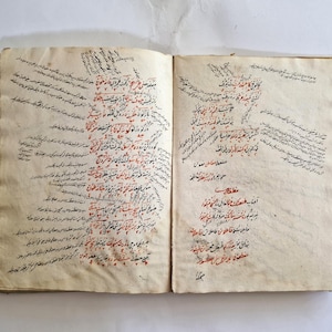 May include: An open book with handwritten text in black and red ink on aged paper. The text is in a flowing script and appears to be in Arabic.