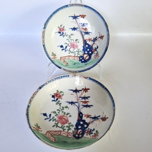 May include: Two white porcelain bowls with blue and red floral designs. The bowls have a green and white border.