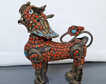 Può includere: Una piccola statuetta di un leone mitologico di colore rosso e oro con accenti turchesi. Il leone è ricoperto di piccole perline rosse e ha un design dettagliato e intricato.