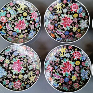 May include: A set of six decorative plates with a black background and a floral design. The plates feature a white rim and a colorful pattern of pink, red, blue, yellow, and green flowers. The plates are arranged in a circular pattern.