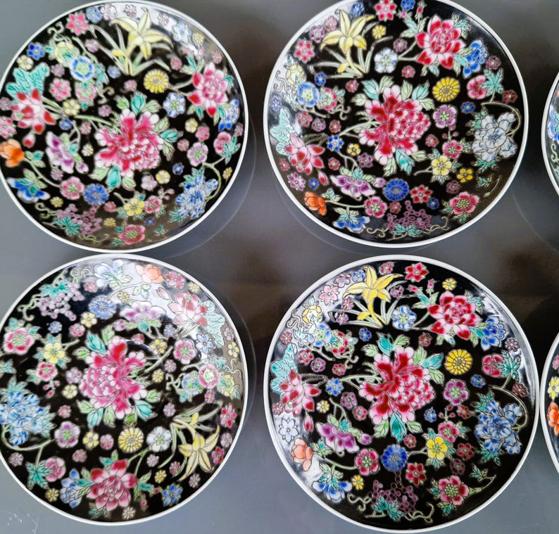May include: A set of six decorative plates with a black background and a floral design. The plates feature a white rim and a colorful pattern of pink, red, blue, yellow, and green flowers. The plates are arranged in a circular pattern.