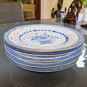 Könnte beinhalten: Ein Stapel von fünf weißen Porzellantellern mit blauen und orangefarbenen Blumendesigns. Jeder Teller hat einen goldenen Rand und einen detaillierten blauen Rand. Die Teller sind übereinander gestapelt.