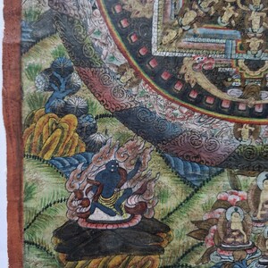 Pu&ograve; includere: Un dipinto di mandala dettagliato su tela, che presenta una divinit&agrave; centrale circondata da intricati motivi e figure. La divinit&agrave; &egrave; raffigurata in uno schema di colori rosso e arancione fuoco, con un viso blu e pi&ugrave; braccia. Il mandala &egrave; incorniciato da un bordo circolare con uno sfondo verde e blu.
