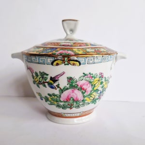 May include: A white porcelain lidded serving bowl with a colorful floral and bird design. The bowl features pink, yellow, and green flowers, with a gold rim and handles. The lid has a small handle and a decorative border.