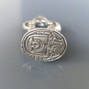May include: An antique silver seal with an oval face and decorative handle. The seal's face has a detailed design with a central emblem and text around the edge. The handle has an ornate, openwork design.