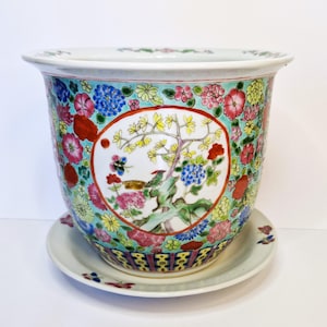 May include: A large, white porcelain planter with a colourful floral and bird design. The planter has a matching saucer.