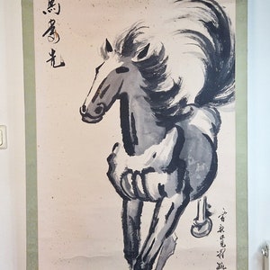 May include: A black and white ink painting on a scroll depicting a horse running with its mane flowing in the wind. The scroll has a green border and the Chinese characters "駿馬" are written in black ink on the left side of the painting.
