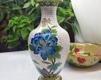 May include: A white porcelain vase with a blue and green floral design. The vase has a gold rim and base.