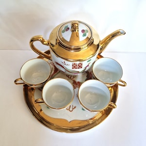 Peut inclure: Un service à thé en or avec une théière et quatre tasses. La théière et les tasses sont décorées d'un dragon et de motifs floraux. L'ensemble est sur un plateau en or.