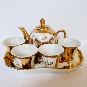 Peut inclure: Un service à thé en or avec une théière et quatre tasses. La théière et les tasses sont décorées d'un motif de dragon rouge et or. L'ensemble est sur un plateau en or.