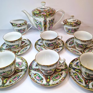 May include: A vintage tea set with a floral pattern in shades of pink, green, and gold. The set includes a teapot, creamer, sugar bowl, and six teacups and saucers.