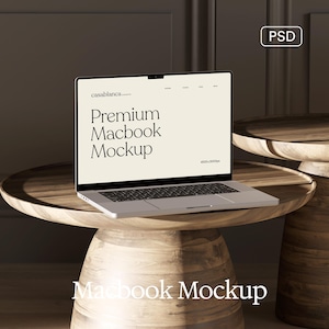 May include: A silver Macbook laptop with a black screen displaying "Premium Macbook Mockup" on a light beige background. The laptop sits on a round wooden table. The image also includes a second wooden table.