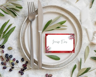 Puede incluir: Tarjeta de lugar de Navidad roja con borde blanco y diseño de rama de acebo verde. La tarjeta dice "Jennifer Elves".