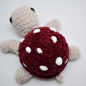 May include: A handmade plush turtle with a burgundy shell dotted with white spots. The turtle's head and limbs are a light beige colour, and it has small black eyes. This soft toy is perfect for children.