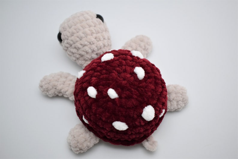 May include: A handmade plush turtle with a burgundy shell dotted with white spots. The turtle's head and limbs are a light beige colour, and it has small black eyes. This soft toy is perfect for children.