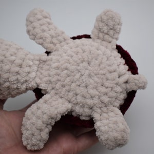 May include: A handmade plush turtle toy. The turtle has a light beige body and limbs, with a dark red shell. The toy is made of a soft, textured material, and is designed to be cuddly.