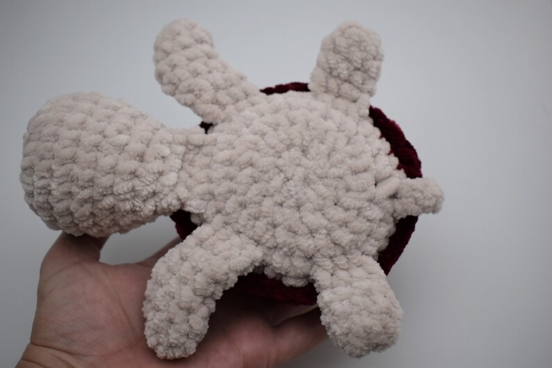 May include: A handmade plush turtle toy. The turtle has a light beige body and limbs, with a dark red shell. The toy is made of a soft, textured material, and is designed to be cuddly.