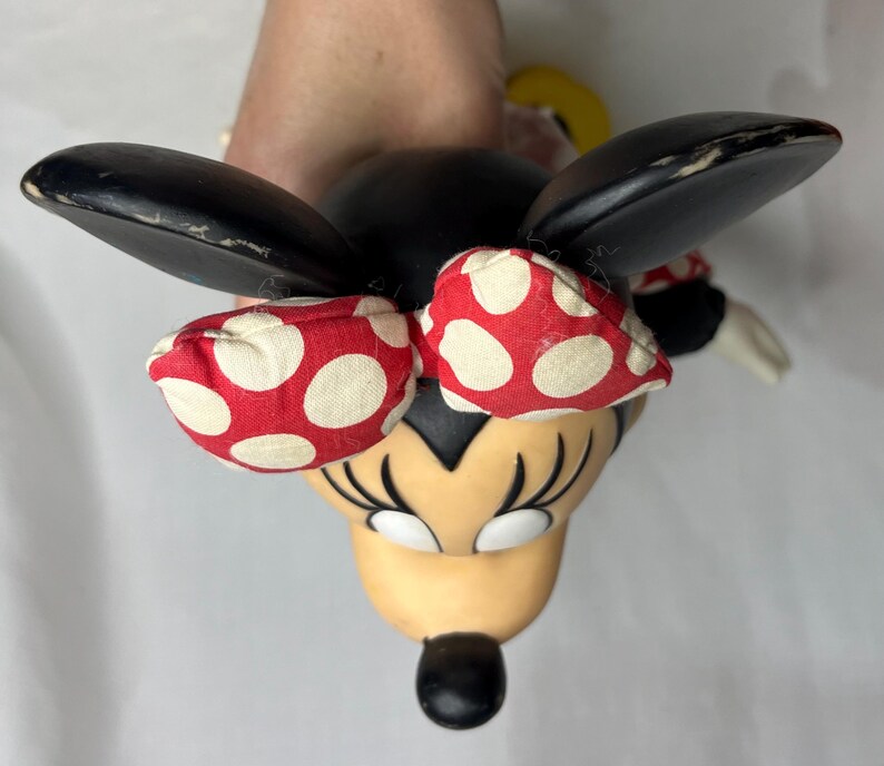 Peut inclure: Figurine de Minnie Mouse avec des oreilles noires, un n&oelig;ud &agrave; pois rouges et blancs et un visage bronz&eacute;. La figurine a des cils noirs et un nez noir. Les oreilles sont l&eacute;g&egrave;rement us&eacute;es.