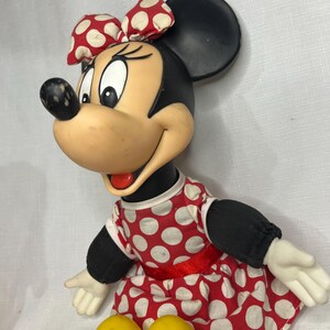 Peut inclure: Poup&eacute;e vintage de Minnie Mouse. La poup&eacute;e a une t&ecirc;te et des oreilles noires, un visage bronz&eacute; et un n&oelig;ud &agrave; pois rouges et blancs. Elle porte une robe &agrave; pois rouges et blancs avec une ceinture rouge et des manches noires. La poup&eacute;e a des chaussures jaunes.