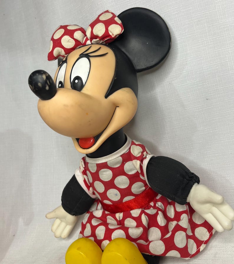 Peut inclure: Poup&eacute;e vintage de Minnie Mouse. La poup&eacute;e a une t&ecirc;te et des oreilles noires, un visage bronz&eacute; et un n&oelig;ud &agrave; pois rouges et blancs. Elle porte une robe &agrave; pois rouges et blancs avec une ceinture rouge et des manches noires. La poup&eacute;e a des chaussures jaunes.