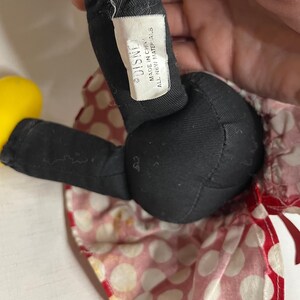 Peut inclure: Gros plan d'une poup&eacute;e en peluche Minnie Mouse. La poup&eacute;e a des jambes noires et un corps noir. La poup&eacute;e porte une jupe &agrave; pois rouges et blancs. L'&eacute;tiquette indique "DISNEY MADE IN CHINA ALL NEW MATERIALS."