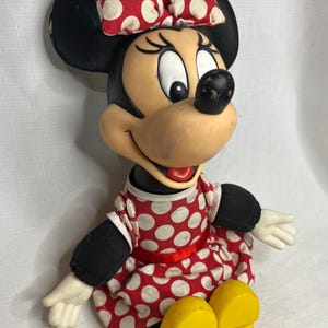 Peut inclure: Figurine de Minnie Mouse, avec une t&ecirc;te et des oreilles noires, un n&oelig;ud &agrave; pois rouges et blancs, et une robe assortie. La figurine a des chaussures jaunes et des gants blancs. Le design est une repr&eacute;sentation classique du personnage de dessin anim&eacute; bien-aim&eacute;.