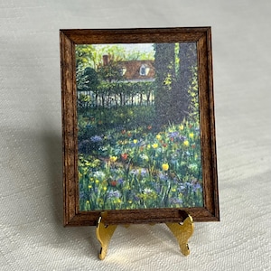 May include: A framed painting of a garden scene with a house in the background. The garden is filled with colorful flowers and greenery. The frame is brown wood and the painting is on a gold easel.
