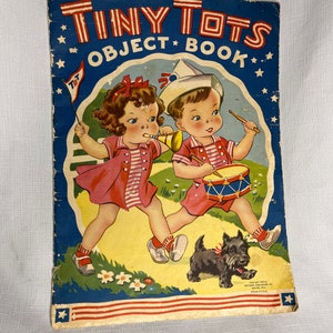 May include: A vintage children's book titled "Tiny Tots Object Book" featuring a colorful illustration of two children playing with musical instruments and a dog. The cover is decorated with stars and stripes.