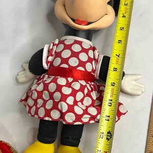 Peut inclure: Poup&eacute;e Minnie Mouse, environ 38 cm de haut, v&ecirc;tue d'une robe &agrave; pois rouges et blancs avec un n&oelig;ud assorti. La poup&eacute;e a des oreilles noires, des jambes noires, des chaussures jaunes et des gants blancs.