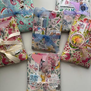May include: Several gift packages wrapped in floral patterned paper, tied with ribbons and twine. Each package contains small items and tags with inspirational quotes. The packages are in various colors, including pink, blue, and green.