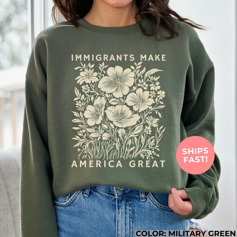 An militry green-colored sweatshirt, illustrating an “Immigrants Make America Great” design with soft pastel flowers—powerful yet gentle, blending activism with beauty to honor the strength, hope, and humanity of immigrant communities.