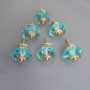May include: Six teal blue glass cabinet knobs with gold accents. Each knob has a scalloped design.